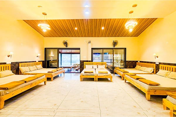 Spacious Maharaja Hall with multiple wooden beds, fresh linens, and ample walking space at Andur Lakeview Resort